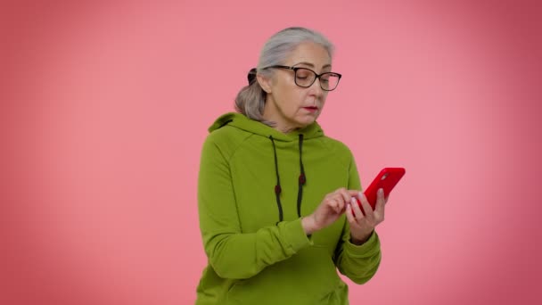 Äldre mormor kvinna använder mobiltelefon surfa på nätet säga wow ja, stora vinna nyheter gör vinnaren gest — Stockvideo