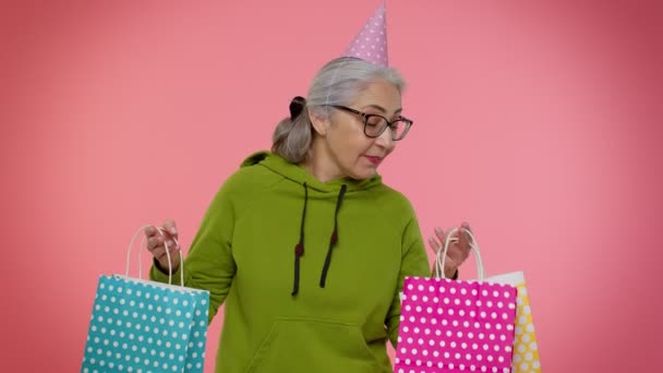 Ηλικιωμένη γιαγιά γυναίκα δείχνει τσάντες ψώνια, διαφημίσεις εκπτώσεις, αναζητούν έκπληκτος με χαμηλές τιμές — Αρχείο Βίντεο