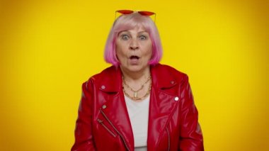 Heyecanlı yaşlı kadın şaşkınlıkla el kaldırıyor kameraya bakıyor, ani bir zaferle şoke oluyor.