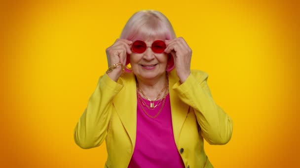Kırmızı güneş gözlüklü, neşeli, yaşlı büyükanne. Göz kırpan göz, gülümseyerek kameraya bakıyor. — Stok video