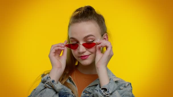 Verleidelijk vrolijk stijlvol meisje in spijkerjasje met zonnebril, charmante glimlach op gele muur — Stockvideo