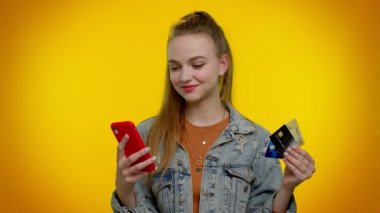 Para transfer ederken kredi kartı ve akıllı telefon kullanan genç bir kız, internetten alışveriş yapıyor.