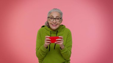 Endişeli yaşlı kadın cep telefonuyla yarış oyunu oynuyor, akıllı telefon sürücüsü simülatörü