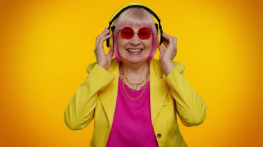 Yaşlı kadın kulaklıkla müzik dinliyor, disko dansı yapıyor, eğleniyor, el kol hareketi yapıyor.