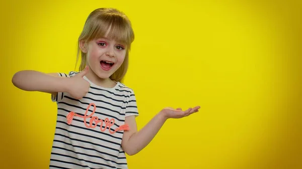 Graciosa niña mostrando pulgares hacia arriba y señalando lugar vacío, área de publicidad para texto comercial —  Fotos de Stock