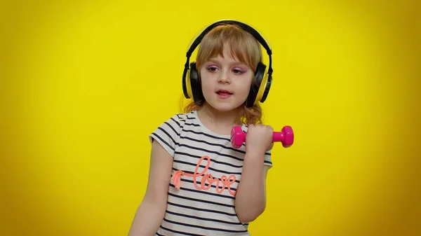 Niña escuchando música a través de auriculares, ejercitando los músculos del brazo levantando pesas rosadas — Foto de Stock