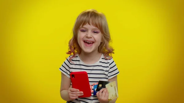 Dziecko dziewczynka używać telefonu komórkowego i plastikowej karty kredytowej, przeglądając powiedzieć wow tak, wielkie zwycięstwo — Zdjęcie stockowe