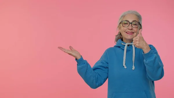 年长的老太太竖起大拇指，指着左边空白的地方，做广告的标志 — 图库照片