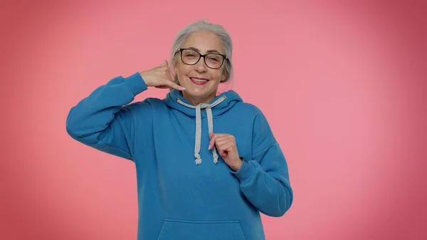 Oudere oma grijs-harige vrouw kijkt naar de camera doet telefoon gebaar als zeg hey bel me terug — Stockfoto