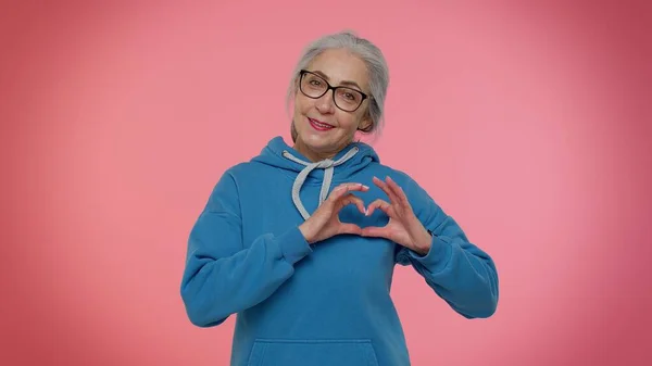 Sorridente donna anziana fa gesto di cuore dimostra segno d'amore esprime buoni sentimenti e simpatia — Foto Stock
