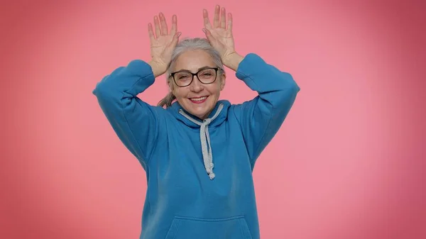 Śmieszne głupie starsza babcia uśmiecha przyjazny i robi królicze uszy gest na głowie, oszukując — Zdjęcie stockowe