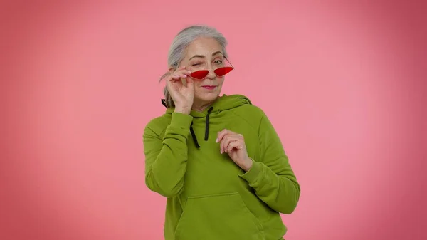 Счастливый игривый пожилой стильный бабуля женщина в солнечных очках моргающий глаз, глядя в камеру с улыбкой — стоковое фото