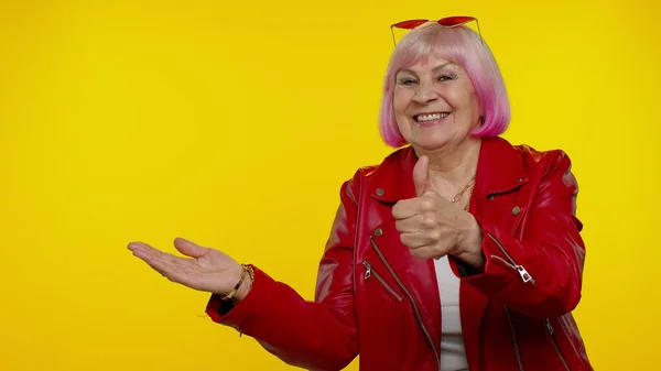 Anciana anciana abuela mostrando pulgares hacia arriba y apuntando a la izquierda en el espacio en blanco, logotipo de la publicidad — Foto de Stock