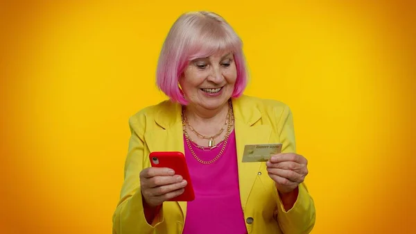 Ältere, stylische Oma kauft mit Kreditkarte und Smartphone online ein — Stockfoto