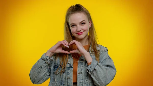 Sonriente adolescente chica hace gesto de corazón demuestra signo de amor expresa buenos sentimientos y simpatía —  Fotos de Stock