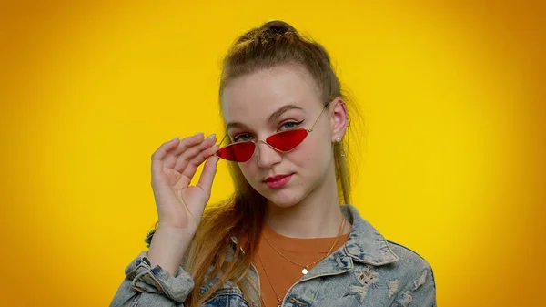 Séduisante fille élégante et joyeuse veste en denim portant des lunettes de soleil, sourire charmant sur le mur jaune — Photo