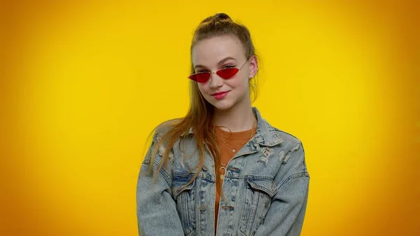 Uwodzicielski wesoły stylowa dziewczyna w dżinsowej kurtce noszenie okularów przeciwsłonecznych, uroczy uśmiech na żółtej ścianie — Zdjęcie stockowe