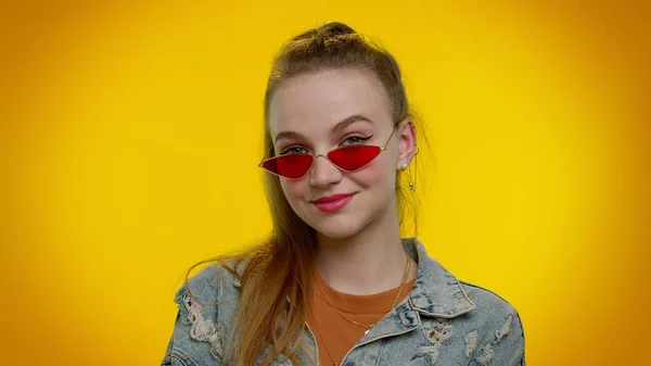 Chica elegante seductora alegre en chaqueta de mezclilla con gafas de sol, sonrisa encantadora en la pared amarilla —  Fotos de Stock