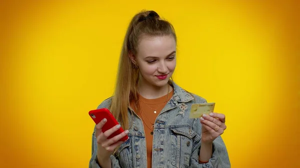 Chica adolescente usando tarjeta bancaria de crédito y teléfono inteligente durante la transferencia de dinero, compras en línea —  Fotos de Stock