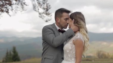 Gelin ve damat kucaklaşıyor, dağ yamacında öpüşüyorlar, düğün çifti