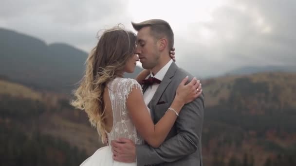 Lovely young newlyweds bride and groom embracing, hugging on mountain slope, wedding couple in love — Stock Video