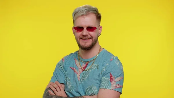 Verführerisch fröhlich stilvoller Mann in blauem T-Shirt mit Sonnenbrille, charmantes Lächeln an gelber Wand — Stockfoto
