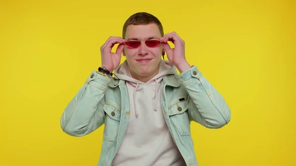 Соблазнительный веселый стильный мужчина в джинсовой куртке в солнечных очках, очаровательная улыбка на желтой стене — стоковое фото