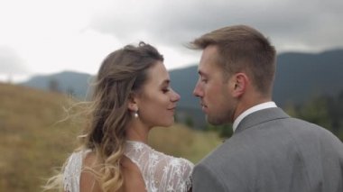 Gelin ve damat kucaklaşıyor, dağ yamacında öpüşüyorlar, düğün çifti