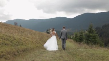 Güzel, genç, yeni evli gelin damat dağ yamacında yürüyor, el ele tutuşuyor, düğün çifti ailesi.