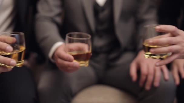 Compañía de novios amigos sosteniendo y tintineando vasos de bebidas alcohólicas de whisky en sus manos — Vídeo de stock