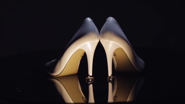 Beautiful women cream-colored evening shoes lie on the floor with two golden wedding rings close-up — Stock Video
