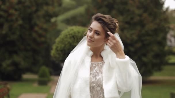 Beautiful and lovely bride in wedding dress and veil in the park waiting for groom. Slow motion — Stock Video