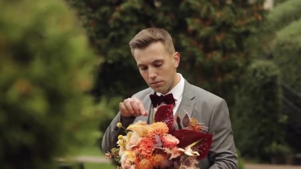 Groom goes down the alley between bushes with a wedding bouquet to his beloved bride, first meeting — Stock Video