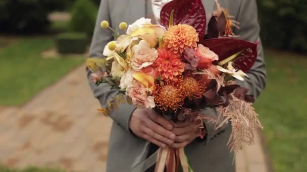 Brudgummen går ner i gränden mellan buskar med en bröllopsbukett till sin älskade brud, första mötet — Stockvideo