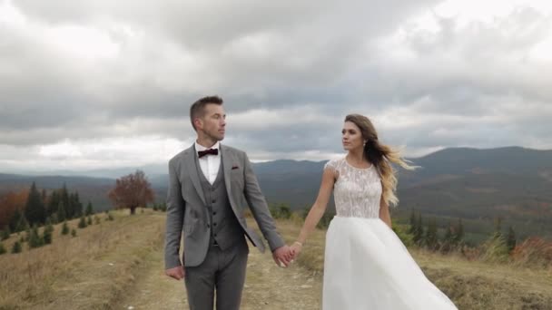 Lovely caucasian wedding newlyweds family bride groom holding hands, making a kiss on mountain slope — Stock Video