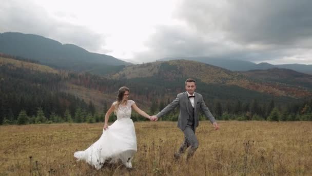 Lovely young newlyweds bride groom running on mountain slope, holding hands, wedding couple family — Stock Video