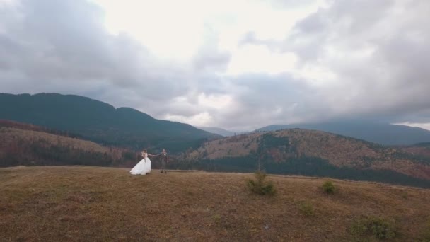 Gyönyörű fiatal friss házasok menyasszony vőlegény séta hegyi lejtőn, légi kilátás, esküvő pár család — Stock videók