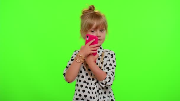 时髦的顽皮的小女孩看着相机，做着电话手势，好像在说：喂，你给我回电话了 — 图库视频影像