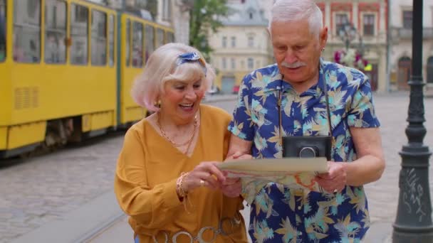 Senior eleganta turister man och kvinna som har en promenad och leta efter sätt att använda papperskarta i gamla stan — Stockvideo