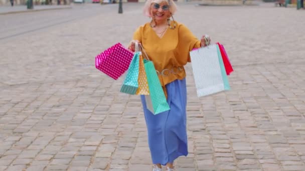 Senior snygg turist kvinna promenader längs gatan i centrum med väskor efter shopping i köpcentret — Stockvideo