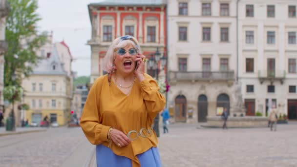 Starsza stara turystka w stylowych ciuchach rozmawiająca przez telefon komórkowy podczas spaceru ulicą miasta — Wideo stockowe