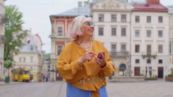 Пожилая стильная туристическая женщина ищет способ найти маршрут с помощью смартфона в старом городе Львов, Украина — стоковое видео