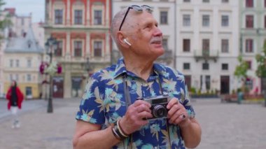 Retro fotoğraf makinesi olan yaşlı bir turist, gülümsüyor, müzik kulaklıkları dinliyor, sokakta dans ediyor.
