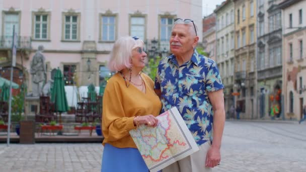 高齢者のスタイリッシュな観光客の男性女性は、古い町で紙の地図を保持し、路上で会話を楽しんで — ストック動画