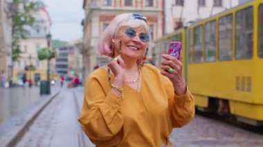 Retro fotoğraf makinesi olan yaşlı bir turist, gülümsüyor, müzik kulaklıkları dinliyor, sokakta dans ediyor.