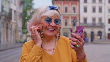 Akıllı telefonlu, gülümseyen, uygulamalı müzik dinleyen, kulaklık takan kıdemli büyükanne kadın turist.