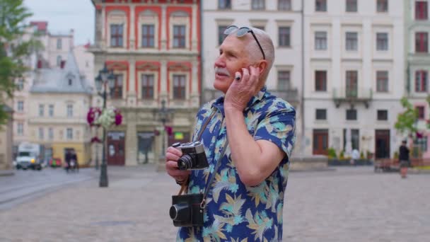 Senior man turist med retro foto kamera, leende, lyssna musik hörlurar, dans på gatan — Stockvideo