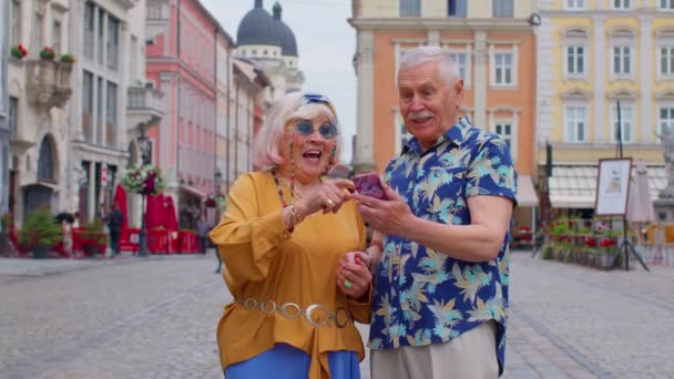 Senior gamla eleganta turister ser smartphone uppriktigt glädje vinna, budskap med goda nyheter — Stockvideo