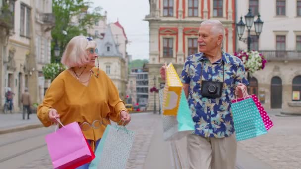 Senior παλιά κομψό τουρίστες άντρας γυναίκα περπατά με πολύχρωμες τσάντες μετά τα ψώνια στο εμπορικό κέντρο στην οδό της πόλης — Αρχείο Βίντεο