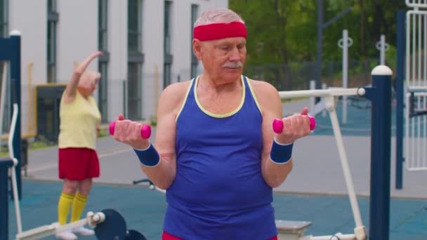 Дедушка-старший занимается тяжелой атлетикой с гантелями на детской площадке в парке — стоковое видео